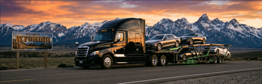 Black semi hauling cars on an open carrier past a Wyoming sign with snow-capped mountains at sunset
