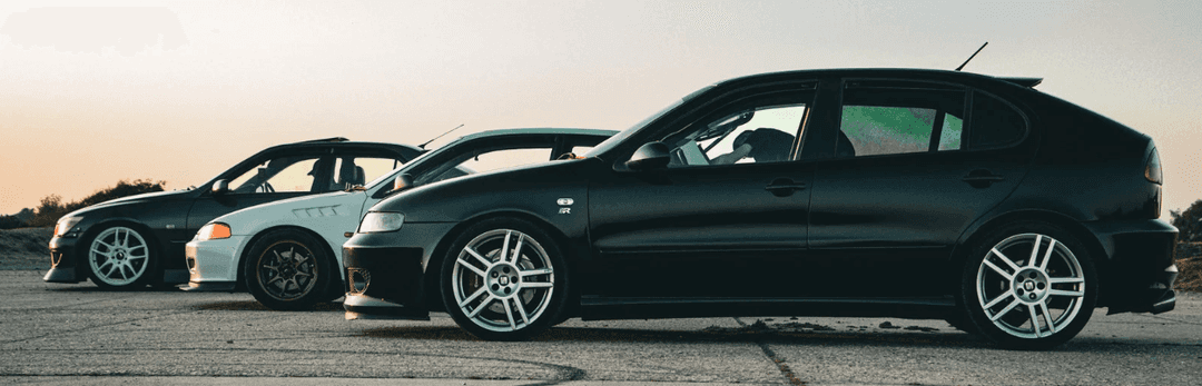 Black hatchback and two other cars parked in a row at sunset