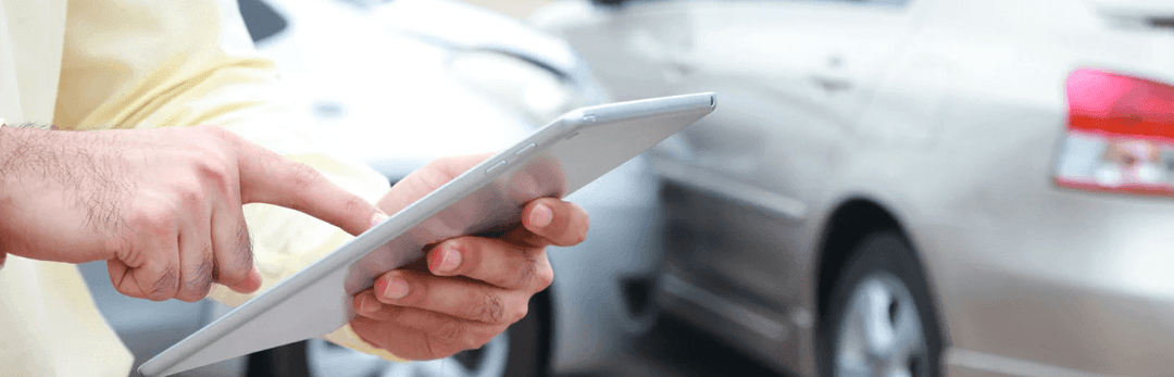Hand holding a tablet next to the side of a silver car to track a shipment