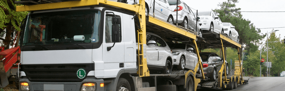 Yellow car carrier truck loaded with white cars on a city street