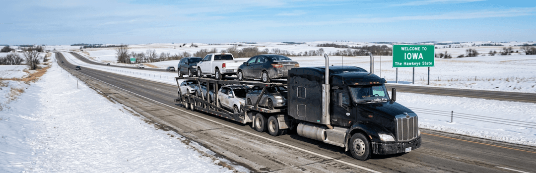 Car carrier truck on a snowy Iowa interstate passing a green Iowa highway sign in winter
