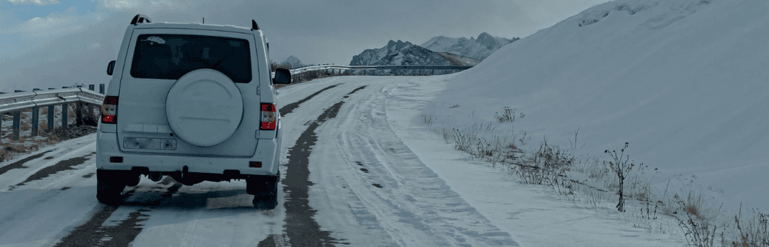 White SUV with a spare wheel cover driving up a snowy mountain road