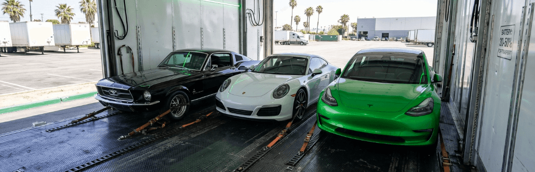 Black classic car, white Porsche and green Tesla secured inside an enclosed car trailer