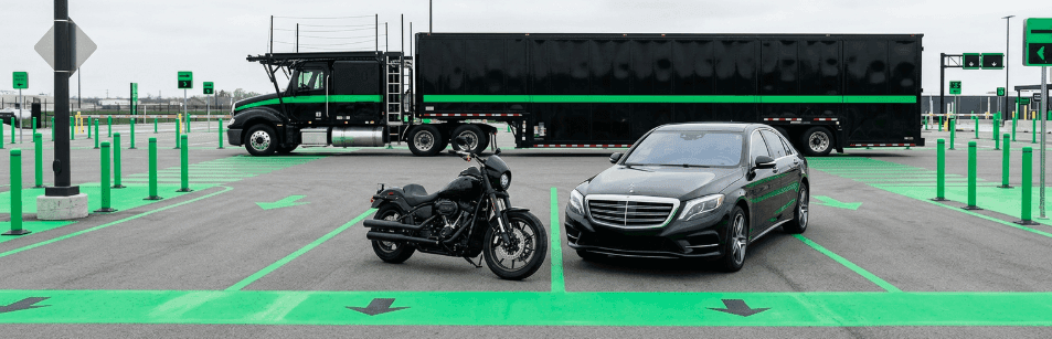 Motorcycle and black sedan parked side by side in marked lanes in front of an enclosed car carrier truck
