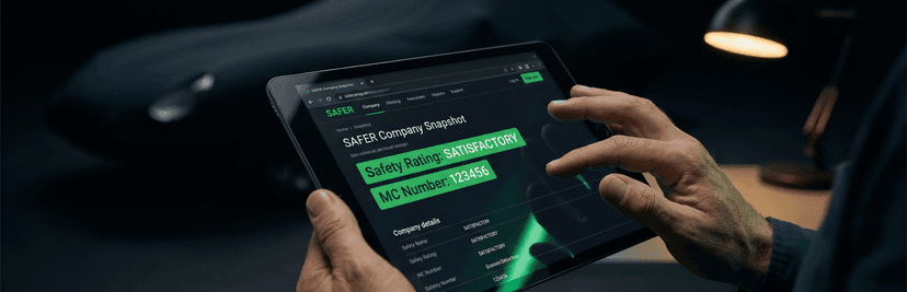 Hands holding a tablet showing an FMCSA SAFER company snapshot with safety rating and MC number highlighted