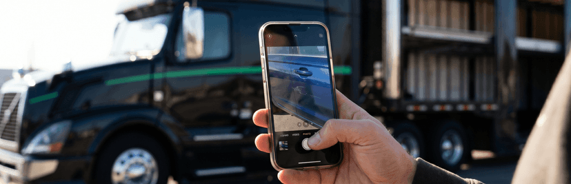 Hand holding a phone photographing a car beside a black car carrier truck before shipping in Mississippi