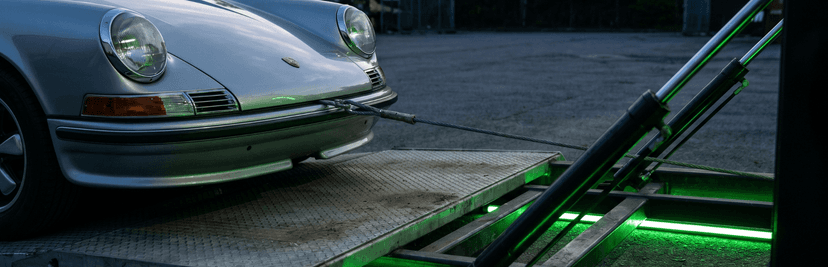 Silver classic Porsche 911 on the ramp of a green-lit enclosed trailer during loading
