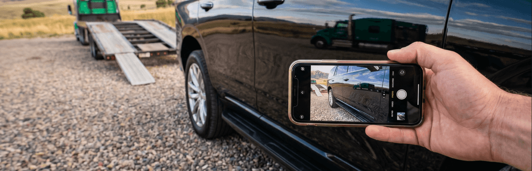 Hand holding a phone photographing the side of a black SUV before it goes up the carrier loading ramps