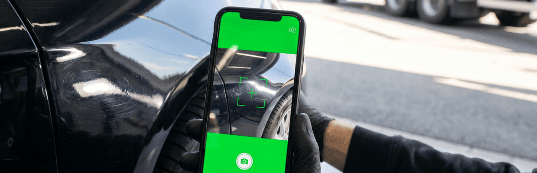 Hand holding a smartphone with a green camera screen, photographing a black car before pickup