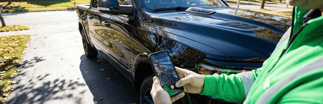 Person in a green jacket photographing a black pickup truck with a phone to document its condition